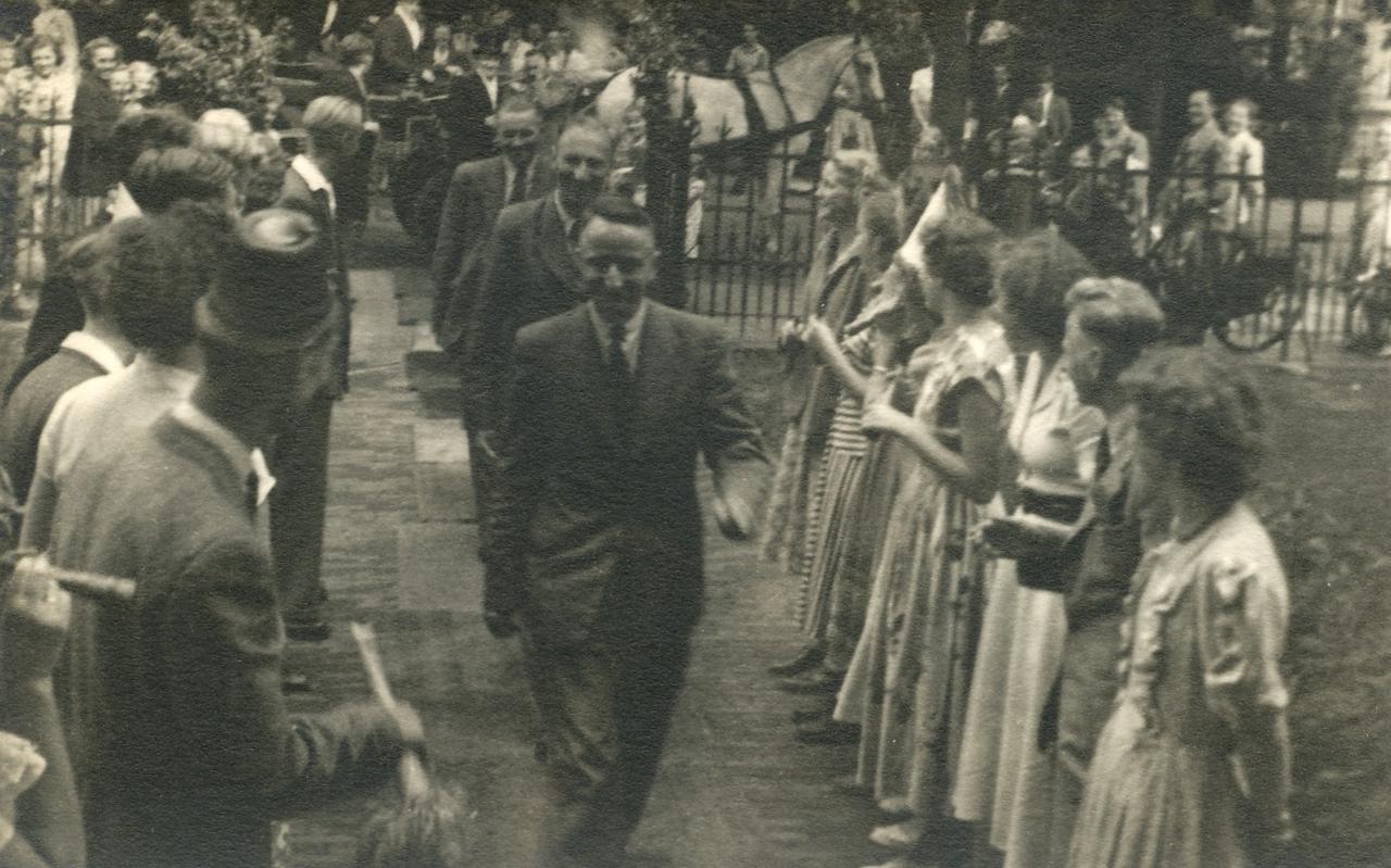 Een leraar loopt door een haag van geslaagde leerlingen naar de ingang van de Rijks HBS.