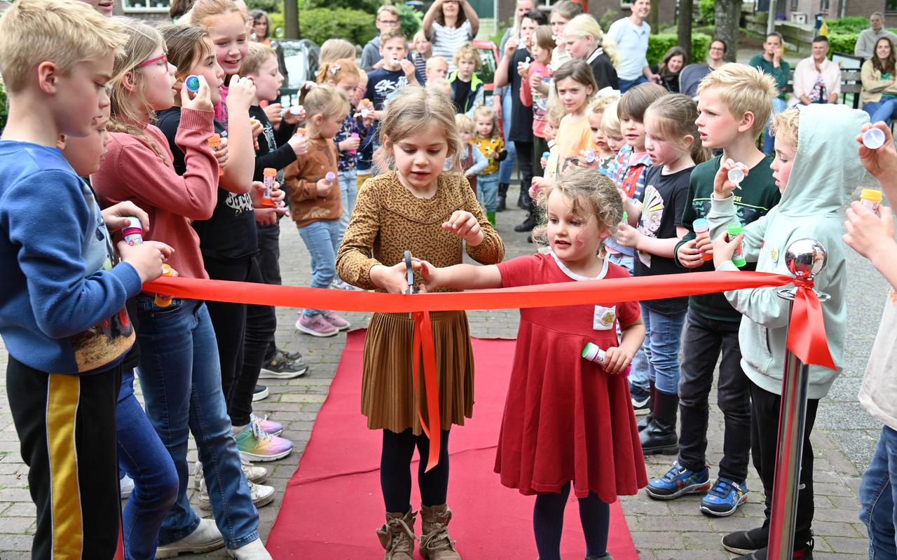 Fenna en Clara proberen samen het rode lint door te knippen, terwijl de andere leerlingen bellen blazen bij de opening van bso De Bosrand in Kerkenveld.