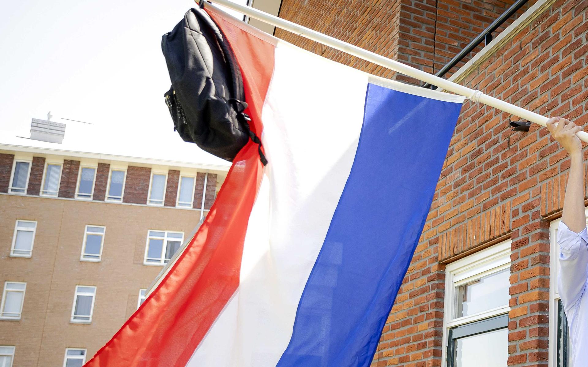 Een gymnasiast hangt zijn tas aan de vlaggenstok nadat hij is geslaagd.